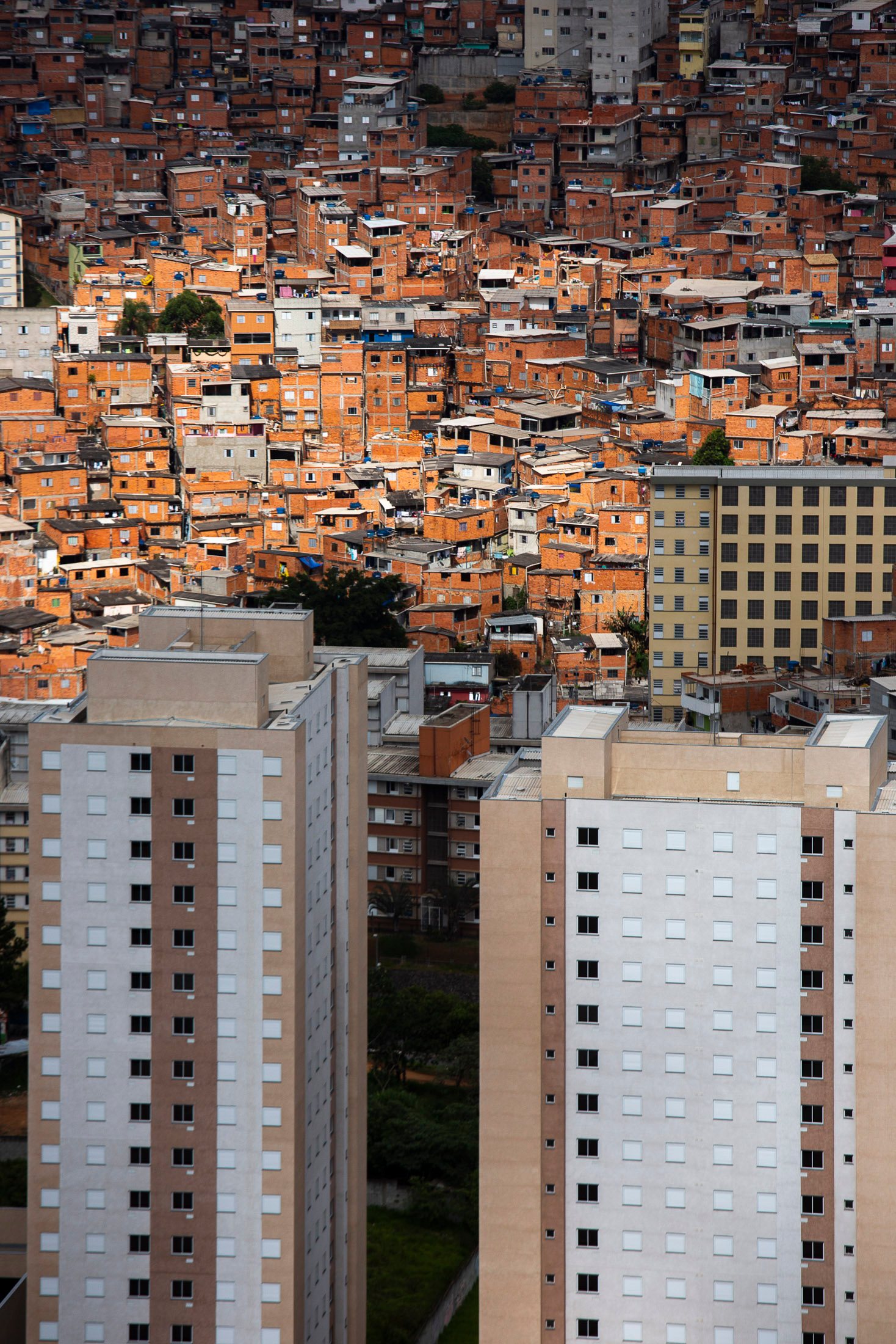 São Paulo favela with orange rooftops clustered behind tall apartment towers.
