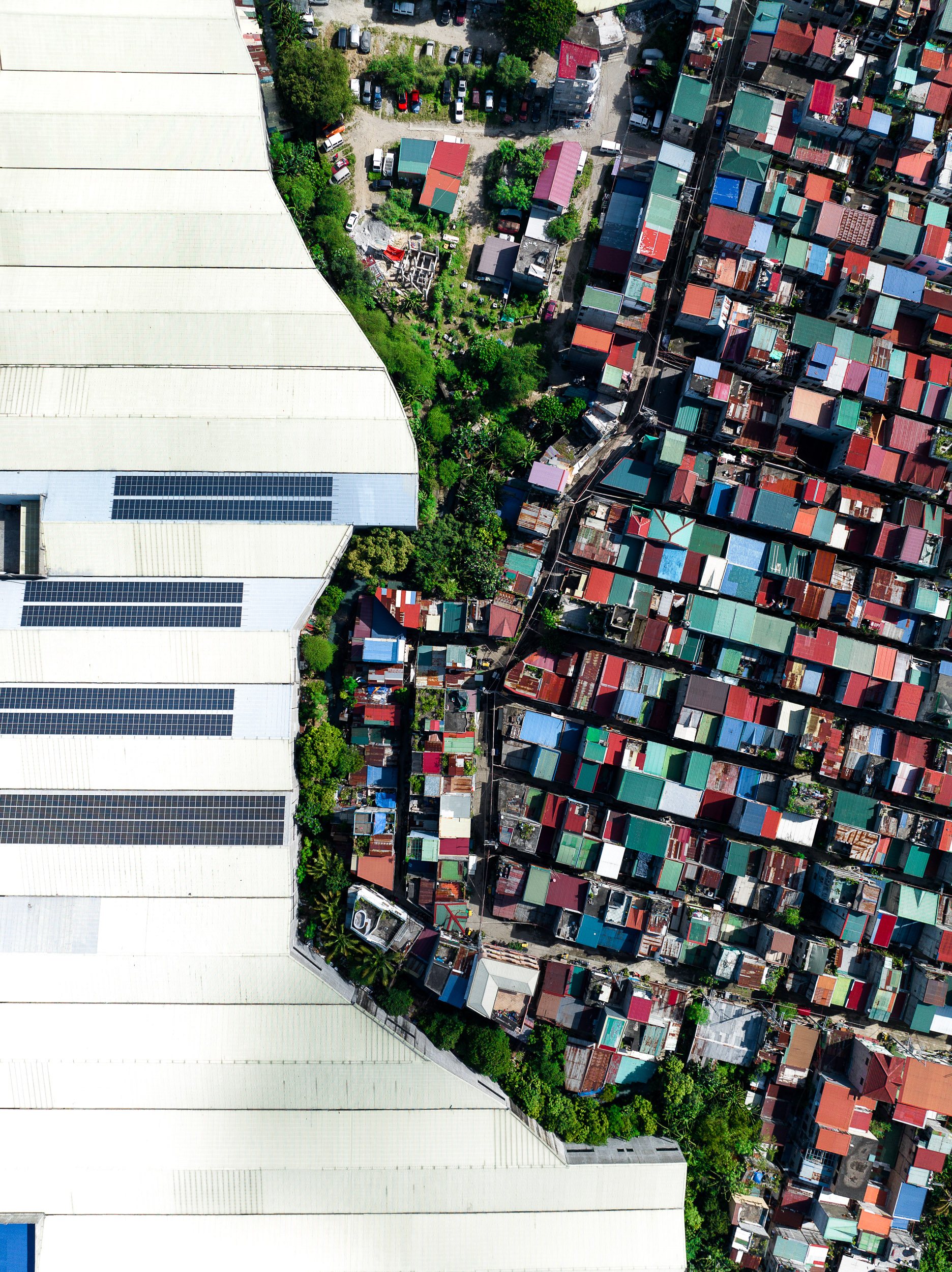Aerial photograph showing warehouse roofs bordering a dense informal community on the outskirts of Metro Manila, near the boundary with Central Luzon.