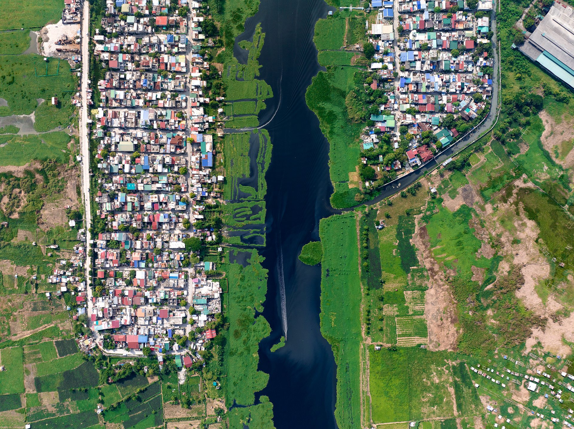 Urban development bordering green floodway in Manila, illustrating spatial contrast and planning tension.