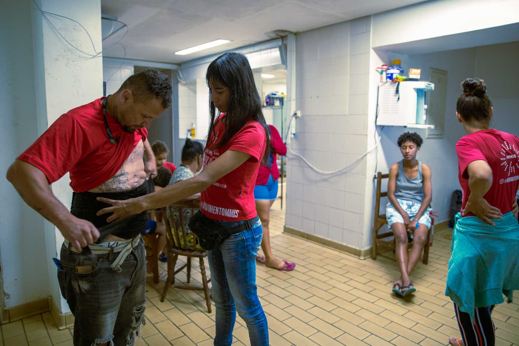 Inside an occupied building in São Paulo, a man named Fabiano receives medical attention from his partner, surrounded by others in a modest, communal space.