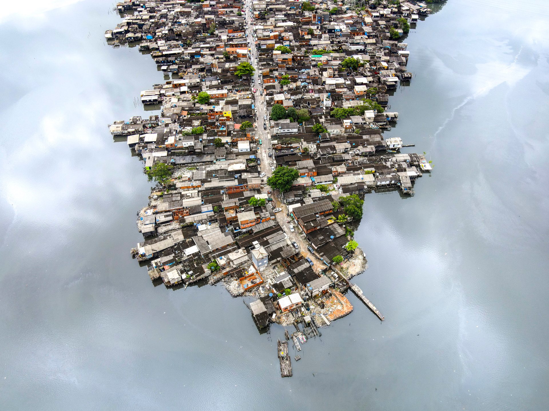 Aerial view of palafitas, or stilt houses, built over water in Santos, Brazil. The homes cluster on a narrow strip of land, illustrating precarious living conditions.