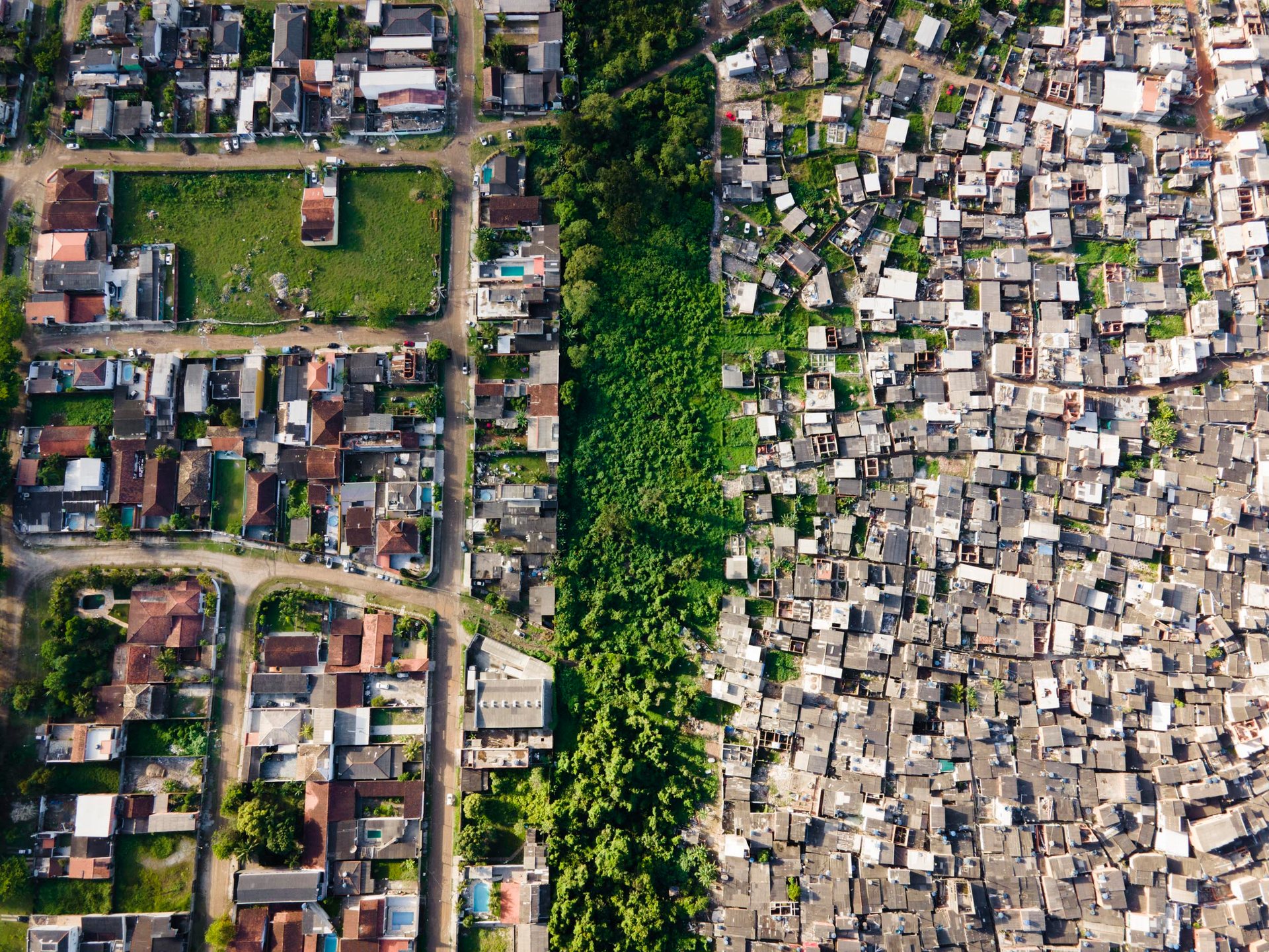 An abrupt line splits the landscape: a densely packed favela borders a lush green suburb, exposing São Paulo’s spatial inequality at the forest edge.